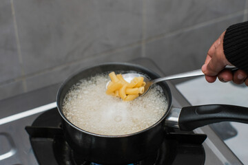 A women cooking the pasta macaroni or penne pasta in wok pan pot in boiling water, cooking pasta homemade.