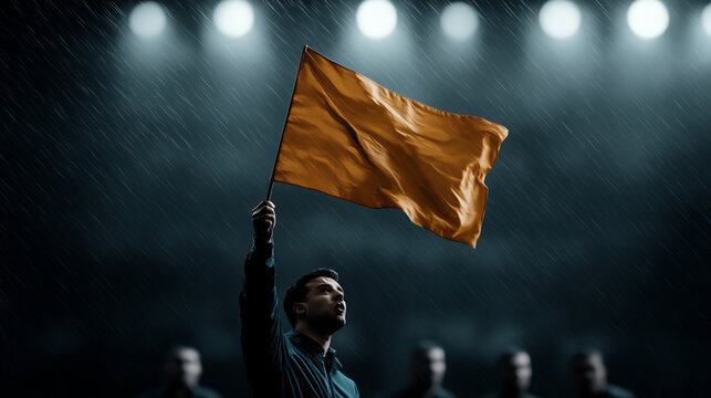 A man raises an orange flag under heavy rain during a night event, surrounded by cheering spectators in a stadium setting