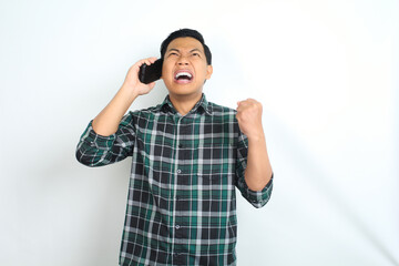 unhappy asian man wearing casual plaid shirt raising his arm show angry face while talking on cellphone isolated on white background