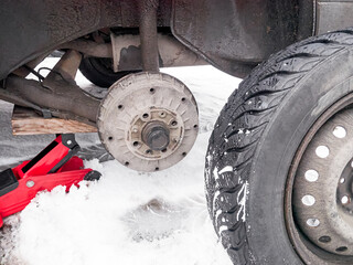 A removed car wheel, a brake disc, an independent wheel replacement. The car is jacked