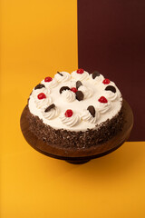 Top view of Chocolate Cake with Whipped Cream and Cherry Topping on brown and yellow background