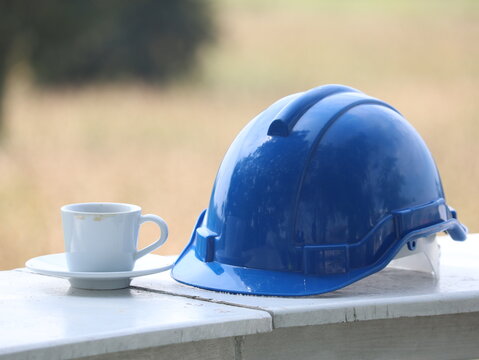 Construction Break: A  blue hard hat sits on a table next to a cup of coffee, symbolizing a moment of respite during a busy construction project.