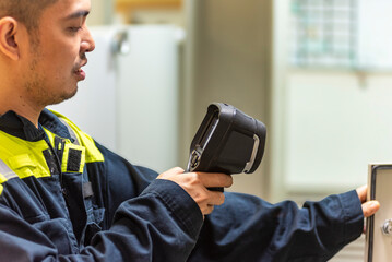 The marine engineer officer uses a thermal camera to inspect electrical equipment, carefully checking for overheating in switch contacts to ensure operational safety and reliability.