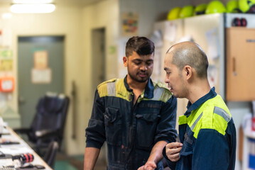 Two marine engineer officers converse in the control room of a merchant vessel, exchanging ideas and organizing tasks for the next day amidst the steady rhythm of operational systems.