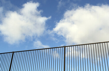 Metal fence against a blue sky with fluffy white clouds textured background abstract