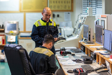 Two marine engineer officers converse in the control room of a merchant vessel, exchanging ideas...