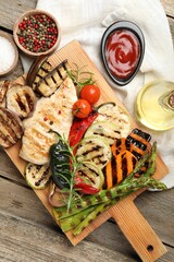 Delicious grilled vegetables and chicken breast served on wooden table, flat lay