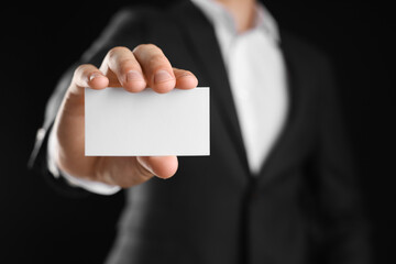 Man holding blank business card on black background, closeup. Mockup for design