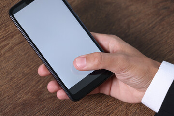 Man unlocking smartphone with fingerprint scanner at wooden table, closeup