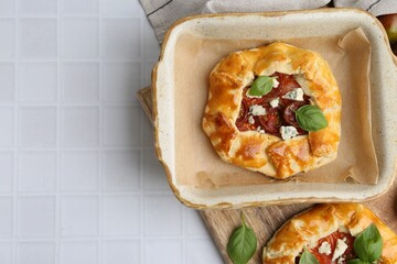 Tasty galettes with tomato, basil and cheese on white tiled table, flat lay. Space for text