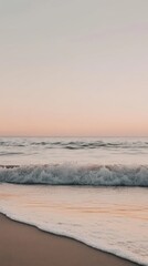 Obraz premium Pastel pink sunset colors the sky over crashing ocean waves on sandy beach