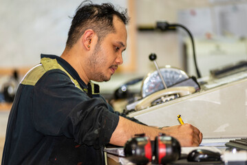 The marine engineer officer sits in the control room of a merchant vessel, focused on recording key operational parameters in the engine logbook, surrounded by monitors displaying system data.