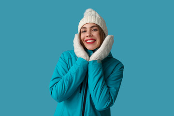 Beautiful young happy woman in warm winter clothes on blue background