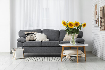 Comfortable sofa and vase with beautiful sunflowers on table in interior of living room