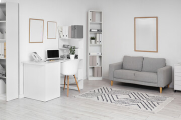 Interior of light office with workplace, sofa and shelf units