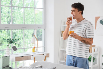 Young man with juice eating tasty muffin at home
