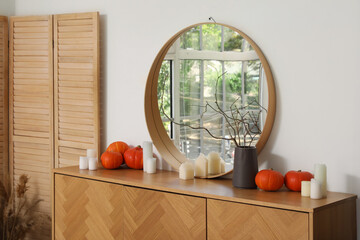 Vase with tree branches, candles and pumpkins on commode in hallway