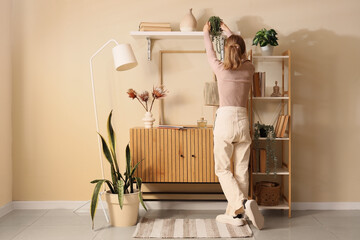 Woman with plant on shelf and commode at home, back view