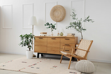 Interior of light room with wooden commode, armchair and plants
