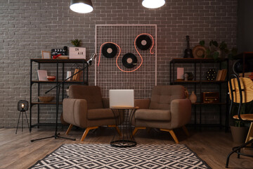 Interior of dark podcaster's studio with armchairs and laptop on table