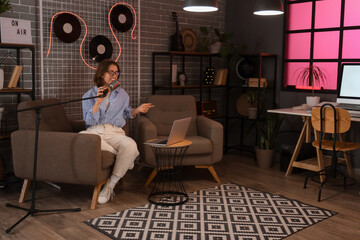 Young woman with microphone and laptop recording podcast in studio