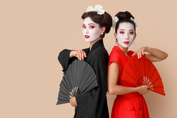Beautiful young geishas with fans on beige background