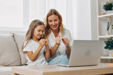 Mother and daughter enjoying quality time together, browsing the internet on a laptop while sitting on a cozy couch
