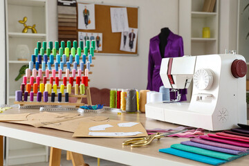 Sewing machine with thread spools and patterns on tailor's table in atelier