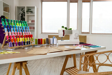 Sewing machine with patterns and thread spools on tailor's table in atelier