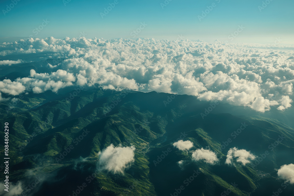 Wall mural Aerial view of lush mountains and clouds under a clear blue sky.