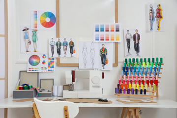 Sewing machine with thread spools and patterns on tailor's table in atelier