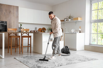 Young man vacuum cleaning carpet in kitchen