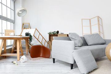 Interior of messy living room with sofa, desk and shelf units after earthquake