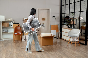 Young businesswoman with lamp and monitor wrapped in stretch film at office on moving day