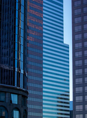 A close-up view of modern office buildings in downtown Los Angeles. The buildings feature sleek glass facades that reflect the surrounding structures, creating an intricate pattern of reflections.