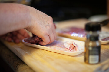 A person skillfully preparing sliced meat on a wooden countertop while seasoning with spices in a cozy kitchen setting