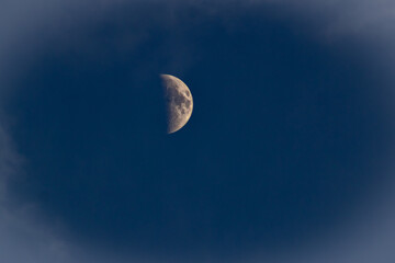 The moon in the dark blue sky with white clouds, closeup