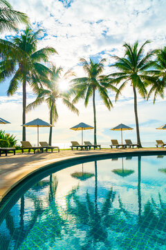 Beautiful luxury umbrella and chair around outdoor swimming pool in hotel and resort with coconut palm tree on blue sky