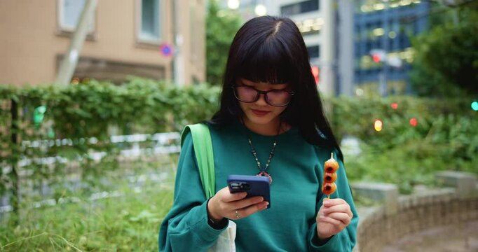 Japanese woman, park and texting with smartphone for social media, mobile notification and dango snack in city. Commuter, phone and search online for travel break, treat or urban street of Tokyo