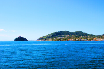 Tidy scenery of Ischia with the large mountainous green island and multicolored buildings connected by a causeway to a volcanic rocky islet with Aragonese Castle and the surrounding Tyrrhenian Sea