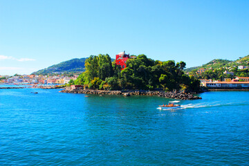 Interesting view from Ischia at the Zoological Station Anton Dohrn - Distaccamento Villa Dohrn, a red building surrounded by trees, the Tyrrhenian Sea, a lone tourist boat and San Pietro beach