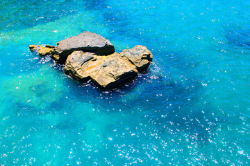 Scintillating view from Ischia at a rugged uneven rock coming out of the Tyrrhenian Sea with its transparent, sparkling, shining, refreshing waters and a blurred vision of the sea bed underneath