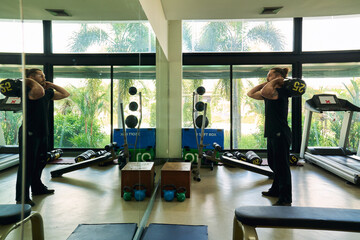 A caucasian handsome man in black shirt workout with weight training in sport gym.