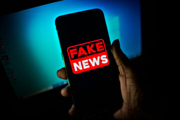Hand holds a smartphone where the phrase fake news appears on the screen