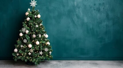Christmas tree with white and silver ornaments against a teal wall.
