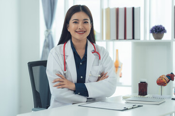 Confident Doctor: A friendly Asian female doctor sits at her desk in a well-lit office, radiating warmth and professionalism. She wears a white coat with a stethoscope.