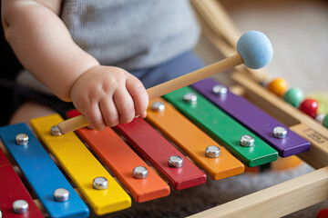 Baby hand holding hammer playing colorful xylophone, musical toy