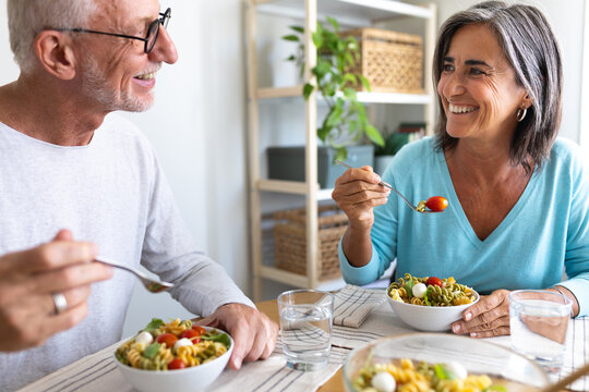 Mature married couple enjoying pasta salad for lunch. Couple looking at each other smiling while eating.