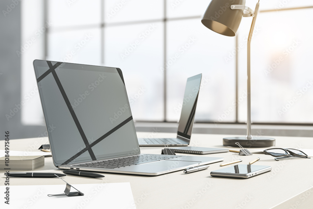 Poster perspective view on stylish sunlit workspace with modern laptops with reflection, smartphone, lamp a