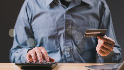 A man is holding a credit card and using a calculator